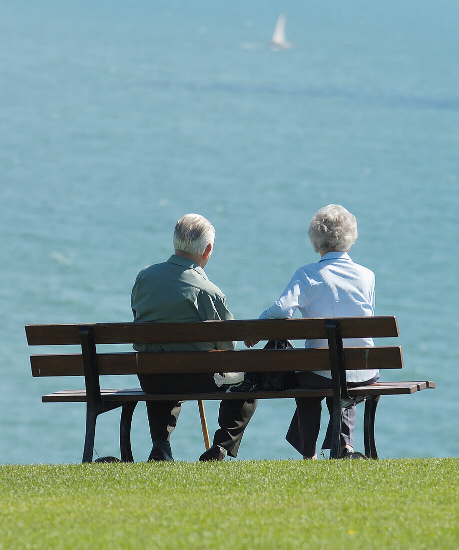 Ein älteres Ehepaar sitzt auf einer Bank und schaut aufs Meer hinaus