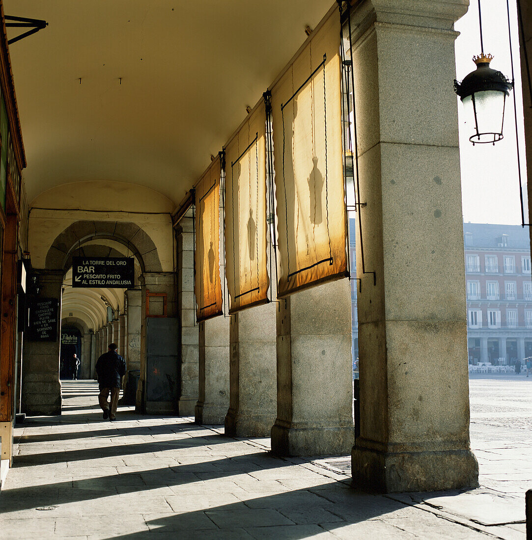 Mann geht neben der Kolonnade auf der Plaza Major spazieren