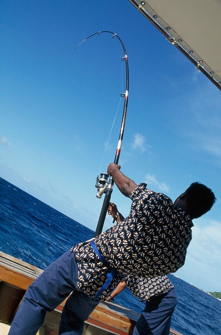 Bootsmann mit Angelrute beim Einholen des Fangs