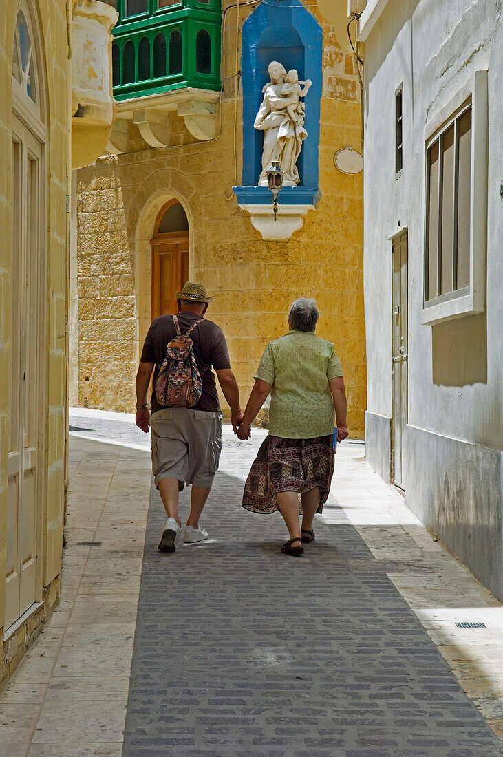 Touristenpaar hält sich an den Händen und geht auf einer schmalen Straße spazieren
