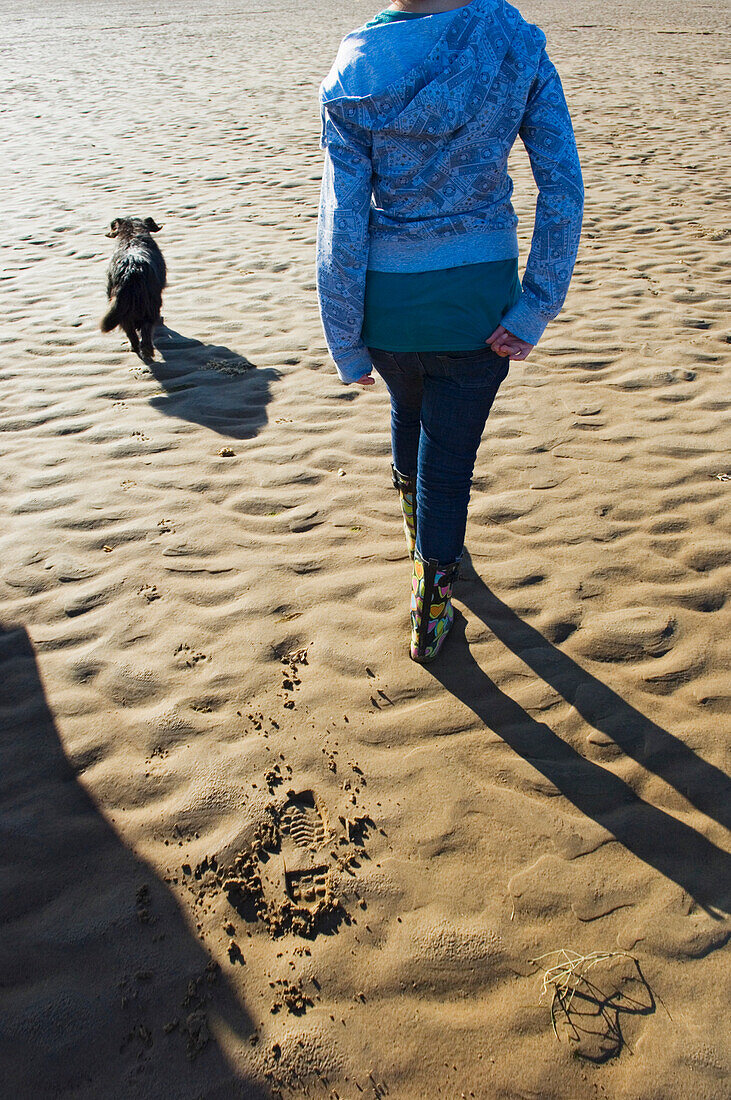 Niedriger Ausschnitt eines jugendlichen Mädchens, das mit ihrem Hund am Strand spazieren geht.