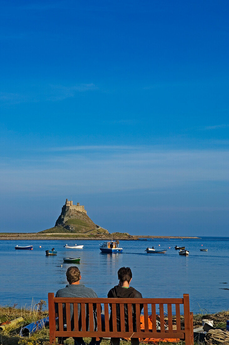 Ehepaar auf einer Bank mit Blick auf Lindisfarne Castle.