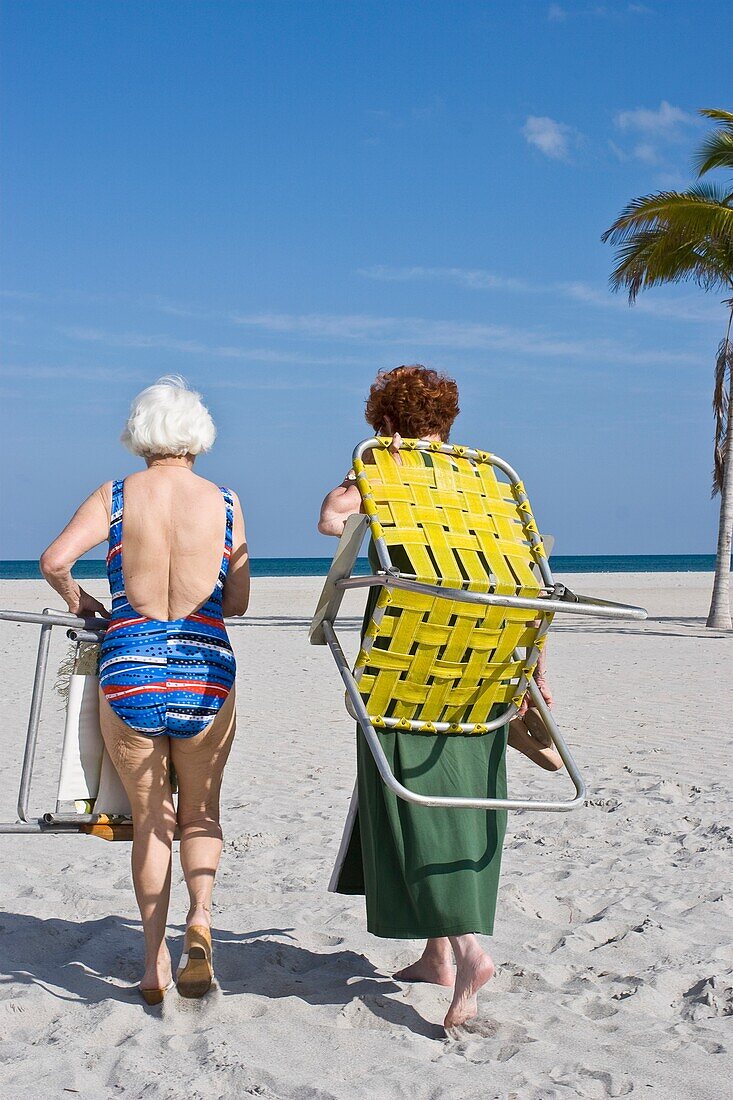 Ältere Frauen tragen Liegestühle am Strand