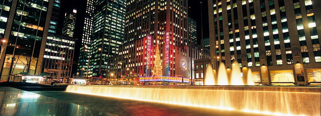 Springbrunnen auf der Sixth Avenue mit Radio City Music Hall und Rockefeller Center bei Nacht