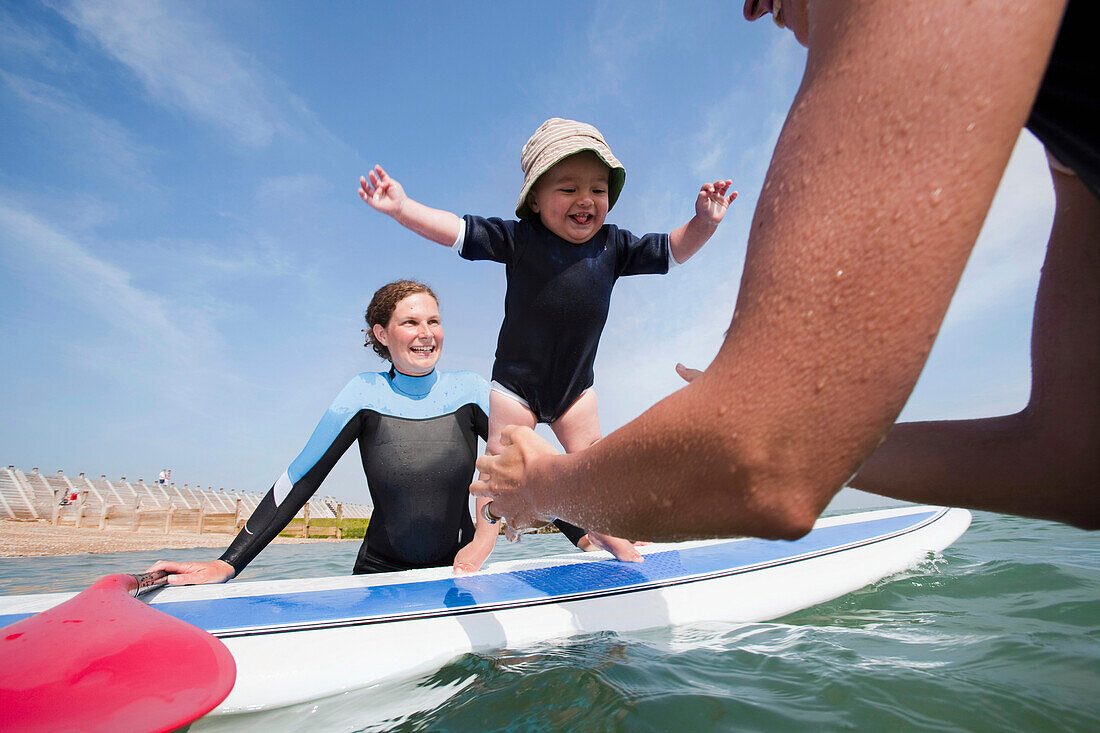 Two Young Women And One Year Old Toddler Playing With A Standup Paddleboard Off The Beachfront At Hayling Island