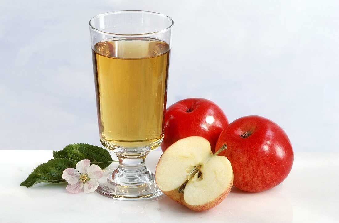 A glass of apple juice, with apples, apple halves & blossom