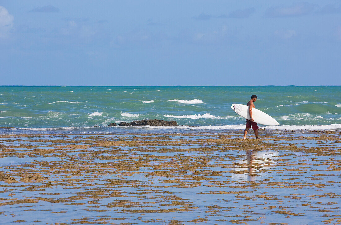 Mann trägt Surfbrett am Praia Do Forte, Bahia, Brasilien