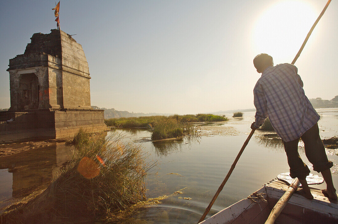 Mann in Boot fährt auf Narmada Fluss in der Nähe von Tempelruinen, Rückansicht, Maheshwar, Madhya Pradesh, Indien