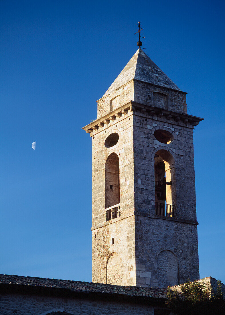 Der Glockenturm der Kirche von Santo Stefano Di Sessanio mit dem Mond dahinter in der Abenddämmerung, Abruzzen, Italien.