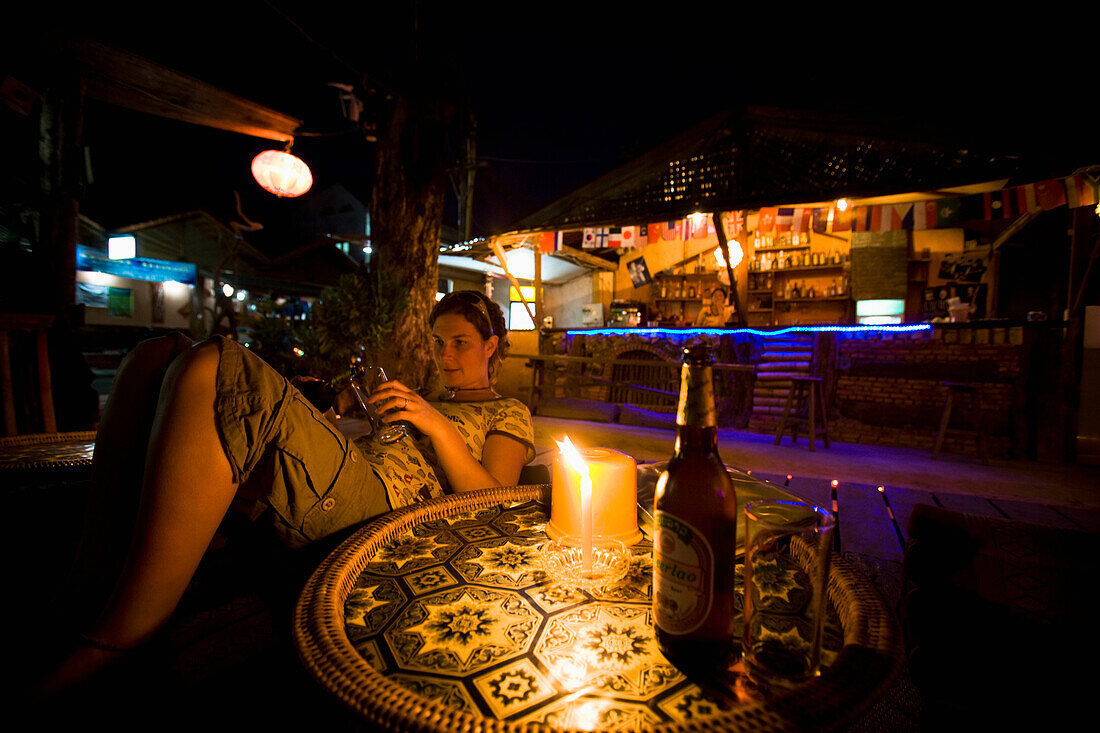 Junge Frau sitzt nachts in einer Bar in Vang Vieng, Laos
