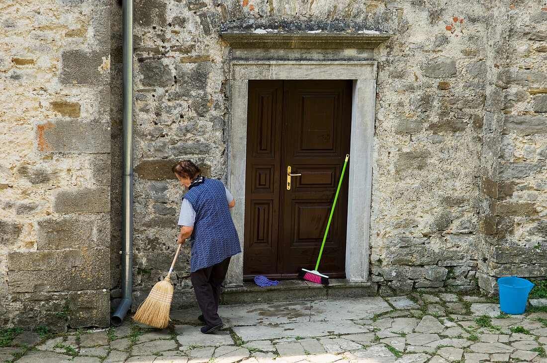 Frau kehrt Straße in der Stadt Hum, Istrien, Kroatien