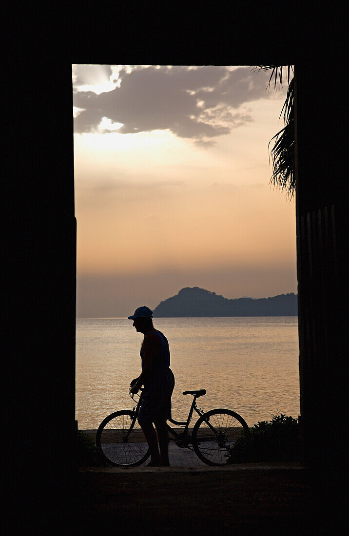 Silhouette Of Man Pushing Bike Along Seafront At Dusk,Side View, Lopud,Croatia