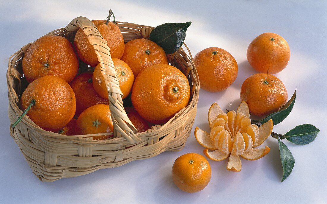 Clementines in a basket with a handle & beside it, one peeled