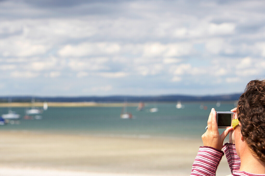 Junge Frau fotografiert am Strand mit Digitalkamera, Chichester Harbour, England, Großbritannien