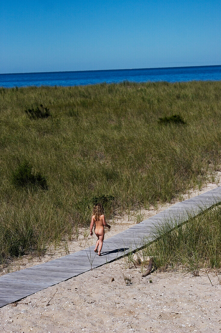 Nacktes Mädchen geht entlang der Uferpromenade in Richtung Meer, Peconic, North Fork, Long Island, New York, USA