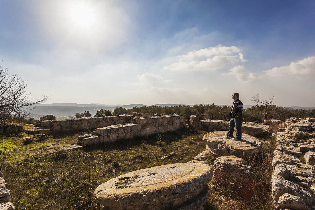 Ein junger Mann steht auf dem Sockel einer Säule an einer Ruinenstätte; Sabasita, Samaria, Israel.
