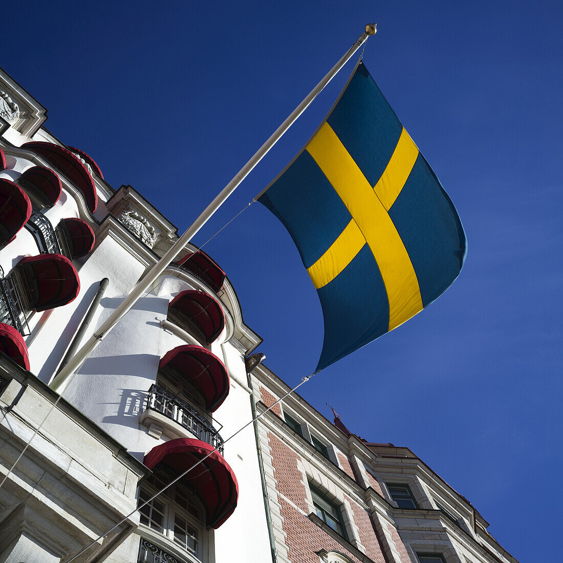 Niedriger Blickwinkel auf die schwedische Flagge und ein Gebäude mit roten Markisen über den Fenstern, Ostermalm District; Stockholm, Schweden