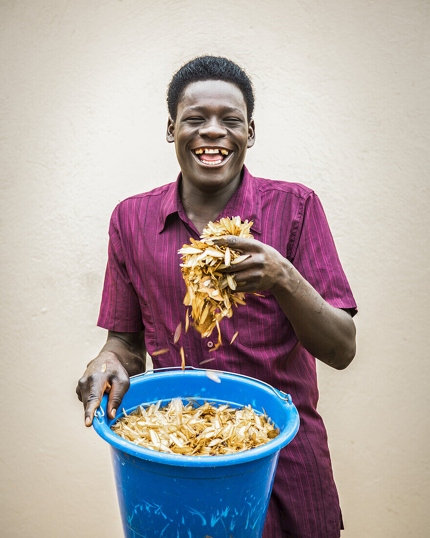 Ein junger Mann hält einen Eimer und eine Handvoll gerösteter weißer Ameisen (Isoptera); Gulu, Uganda.