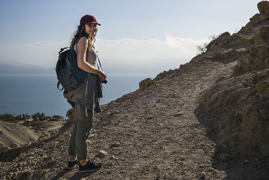 Eine junge Frau posiert beim Wandern in Ein Gedi, mit dem Toten Meer im Hintergrund, Bezirk Totes Meer; Bezirk Süd, Israel.