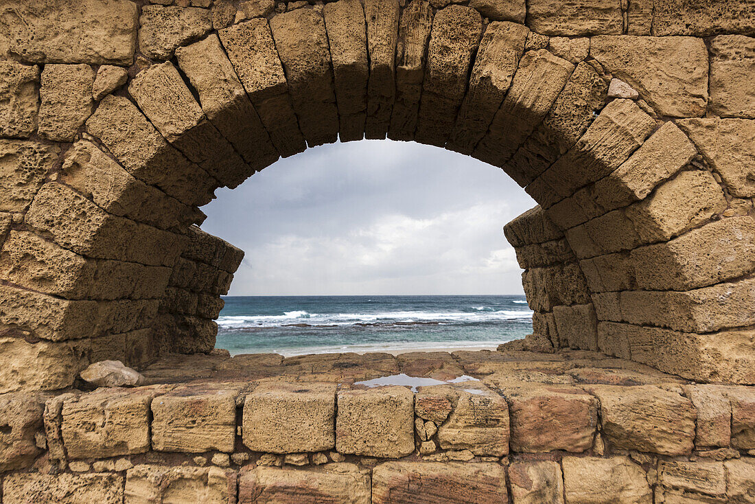 Eine Mauer aus Steinblöcken mit Bogen, die einen Blick auf das Mittelmeer entlang der Küste einrahmt; Jisr Az-Zarqa, Bezirk Haifa, Israel.