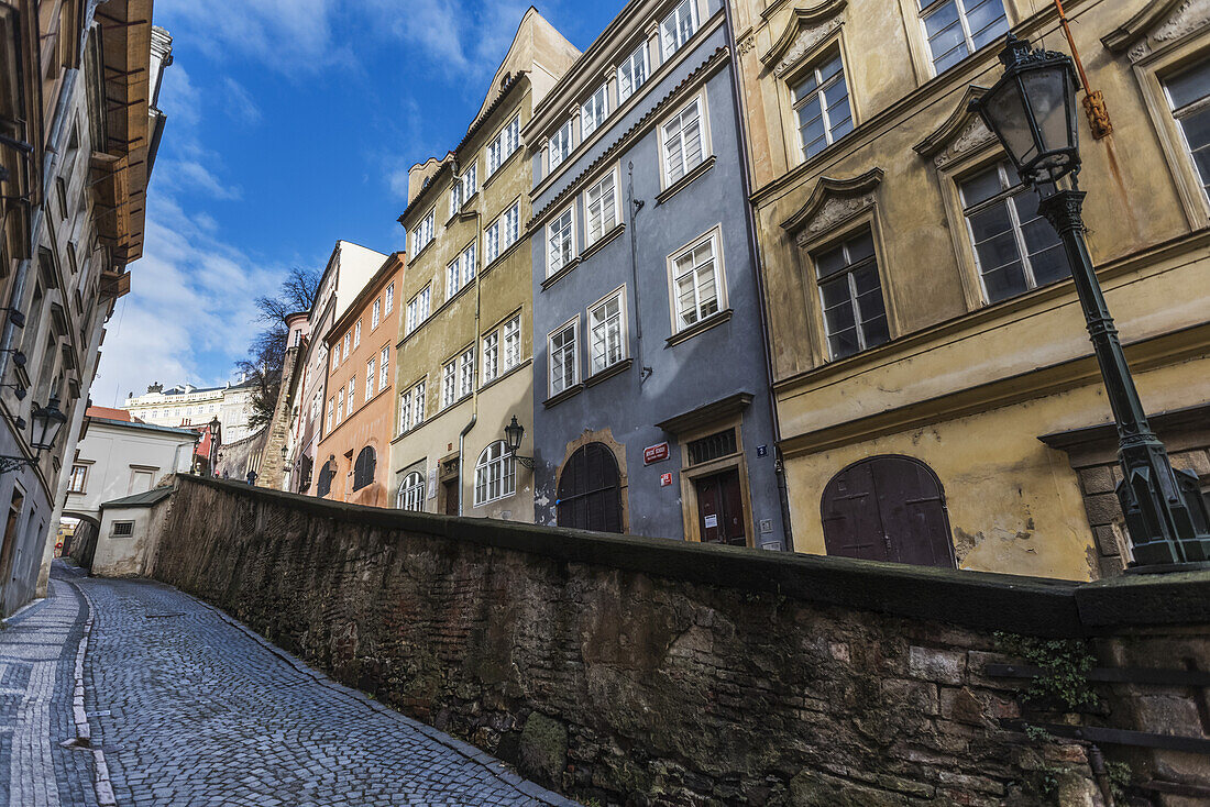 Bunte Wohngebäude und eine Mauer entlang einer schmalen Kopfsteinpflasterstraße; Prag, Tschechien