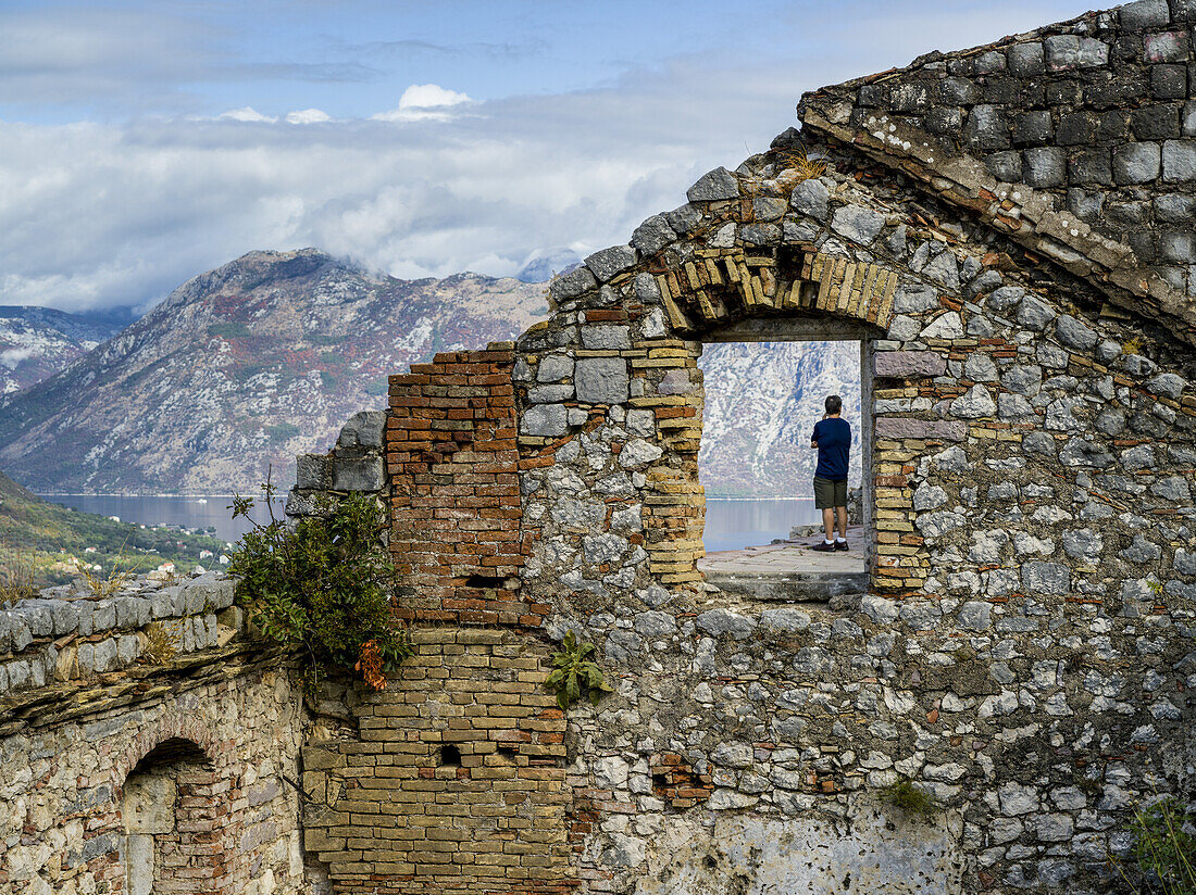 Ein männlicher Tourist steht vor der Burg San Giovanni in Kotor und blickt auf das Wasser; Kotor, Montenegro.