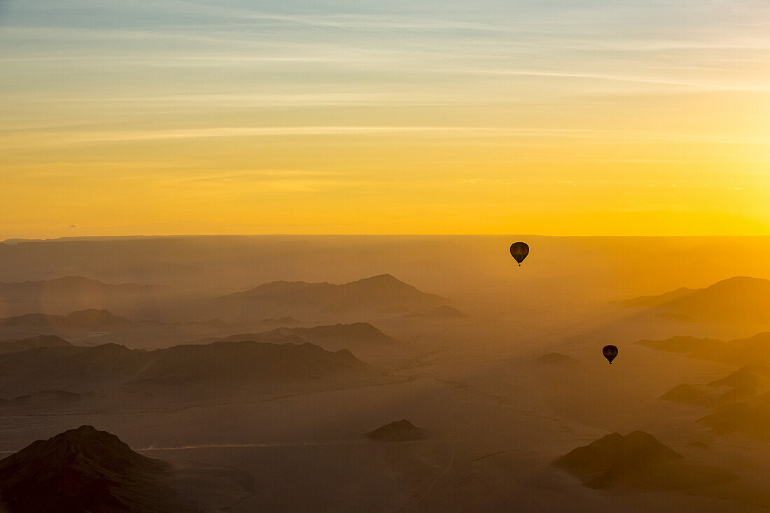 Silhouette of hot air balloons in the golden sky over the sand dunes at sunrise in the Namib Desert; Sossusvlei, Hardap Region, Namibia