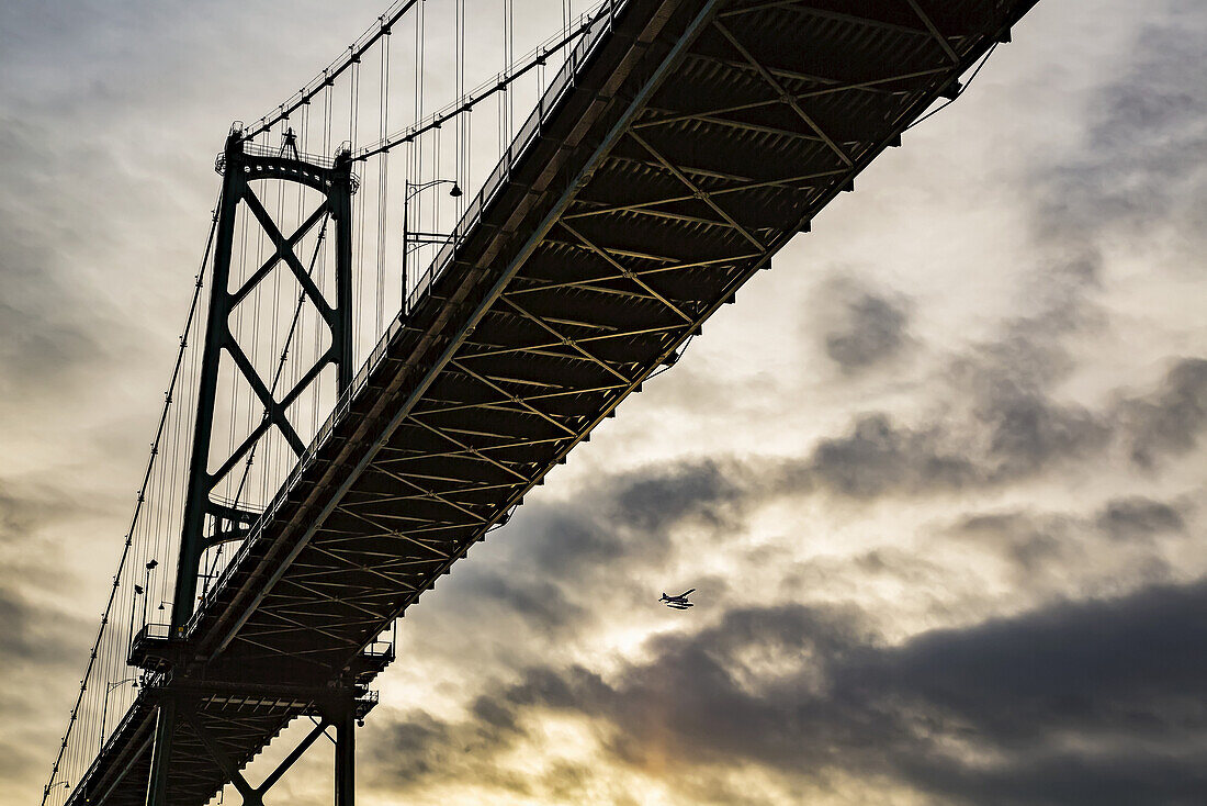 Niedriger Blickwinkel auf eine Brücke bei Sonnenuntergang mit einem Flugzeug in der Ferne; Vancouver, British Columbia, Kanada.