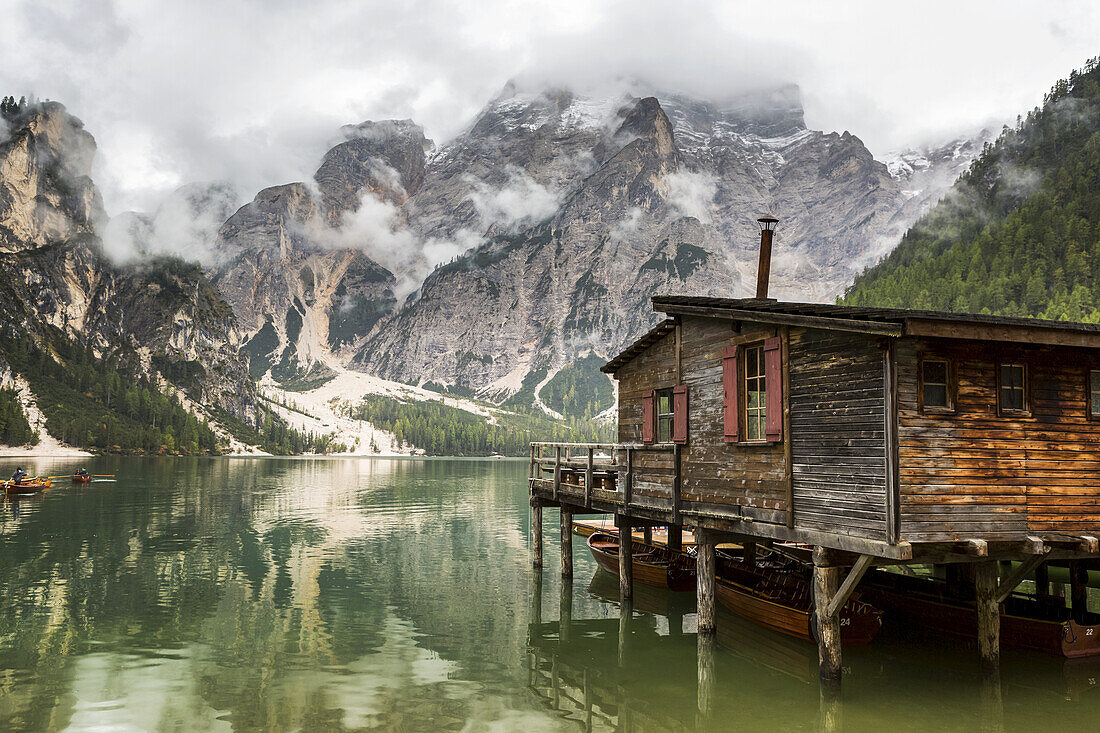 Hölzernes Bootshaus am See mit nebelverhangenem Berg im Hintergrund und Spiegelung im See; Sexten, Bozen, Italien.