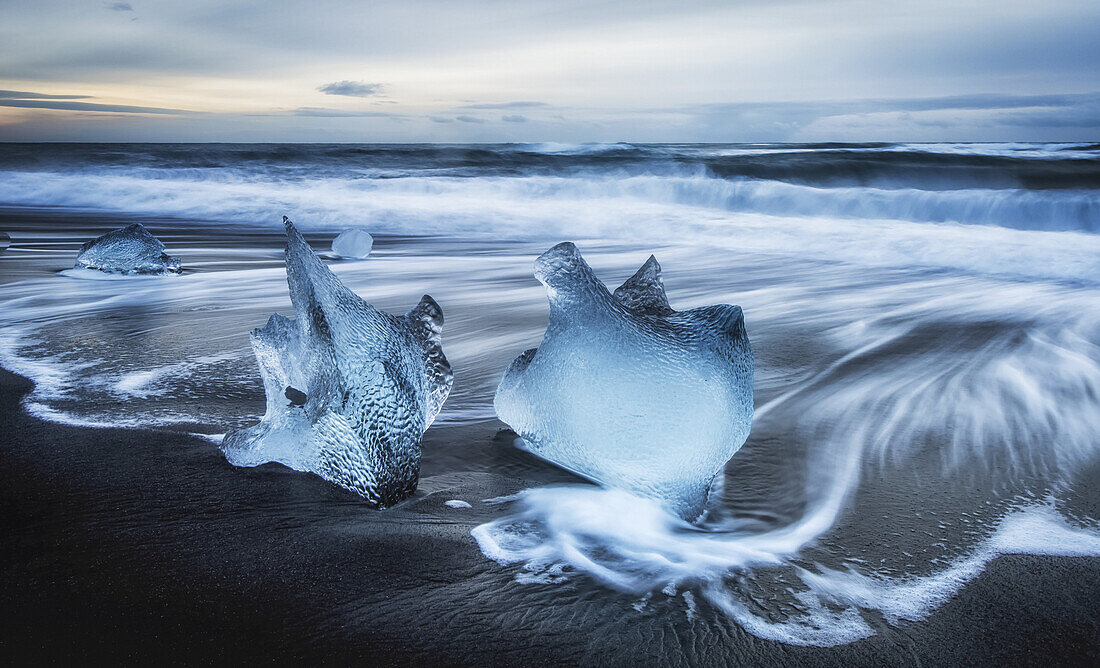 Zerklüftete Eisbrocken liegen auf dem Sandstrand am Rande des Ozeanwassers; Island