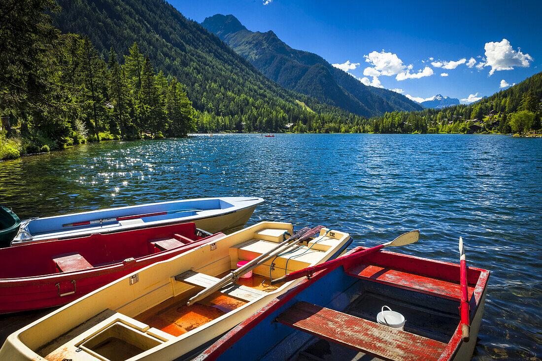 Colourful row boats with Champex Lake surrounded by mountains under blue sky, Alps; Champex, Switzerland