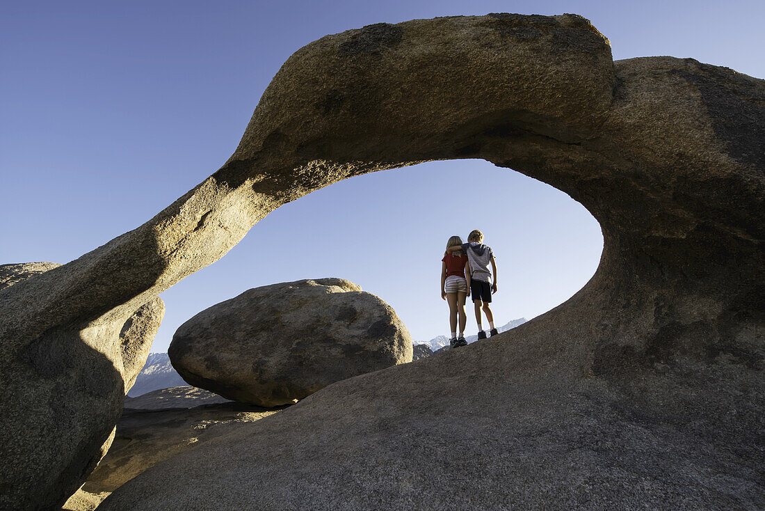Young children standing under a natural rock arch, Alabama Hills; California, United States of America