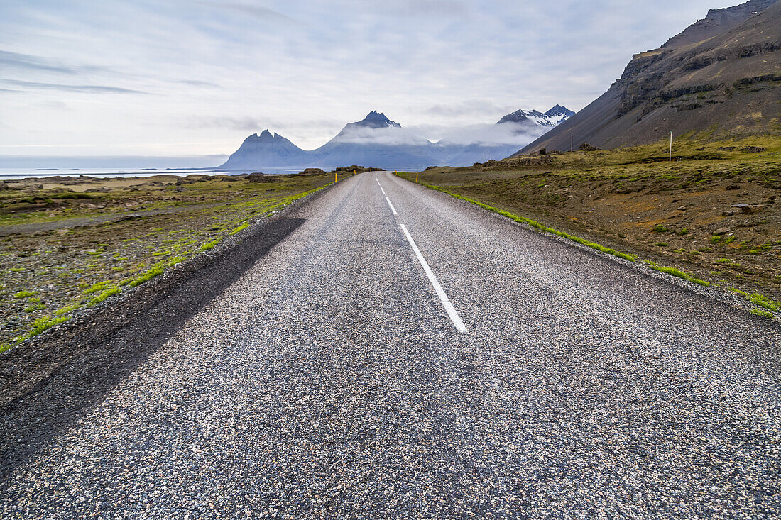 Die lange asphaltierte Straße, die in die vulkanische Berglandschaft in der Ferne führt; Island