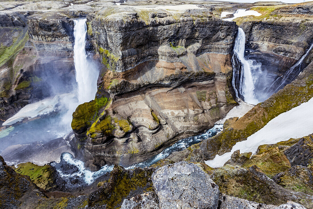 Die atemberaubenden erdigen Farben und Felsformationen zusammen mit dem ungeschmolzenen Schnee, der in der Talsohle des Haifoss zwischen zwei Wasserfällen ruht.  Natürliche Schönheit an einem der besten Aussichtspunkte für Wanderungen in Island; Island