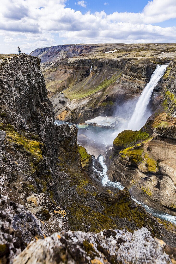 Eine Wanderin posiert am Rande einer hohen Klippe über dem Wasserfalltal von Haifoss; Island.