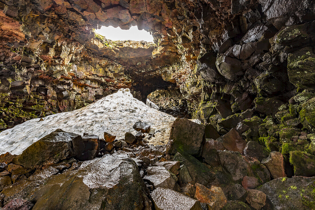 Hiking through the lava tube caves near Reykjavik in early summer, a pile of snow has not quite melted yet from the cave. Visitors here walk the path of lava that flowed during an eruption; Iceland