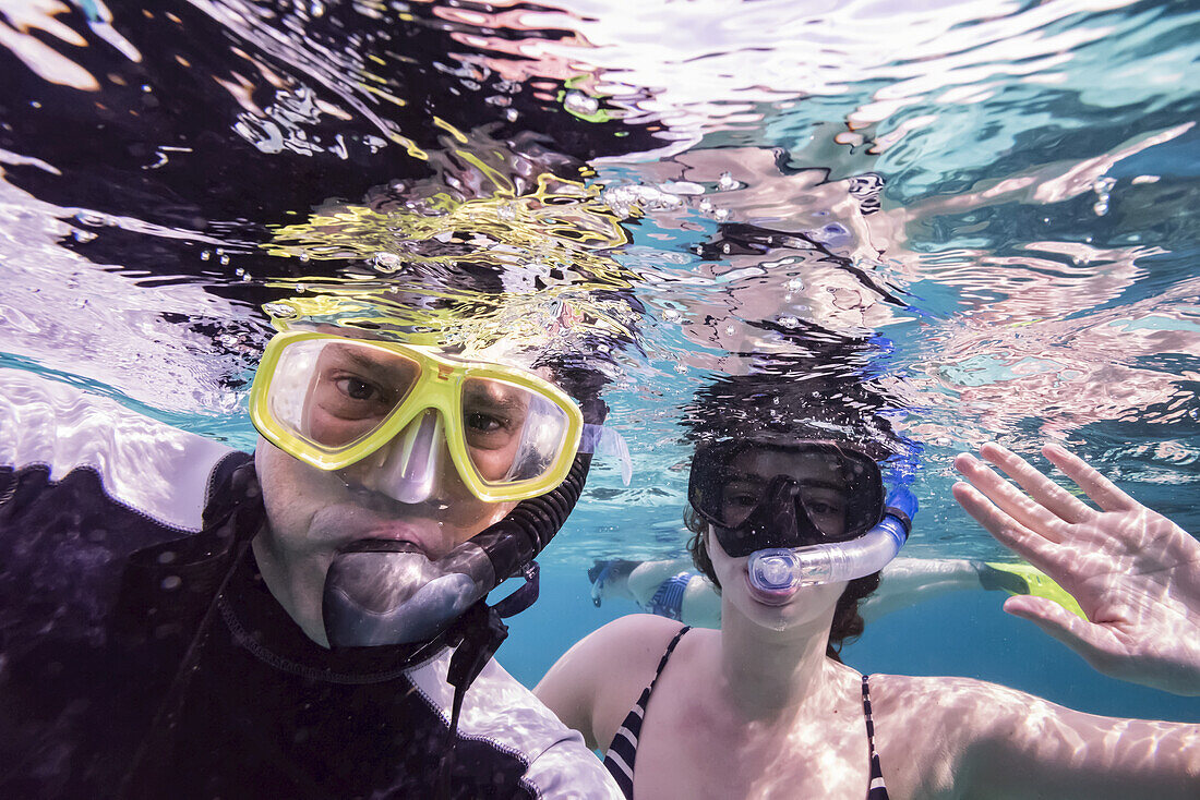 Ein Mann und seine Tochter schnarchen und posieren für die Kamera unter Wasser, Turneffe Atoll; Belize