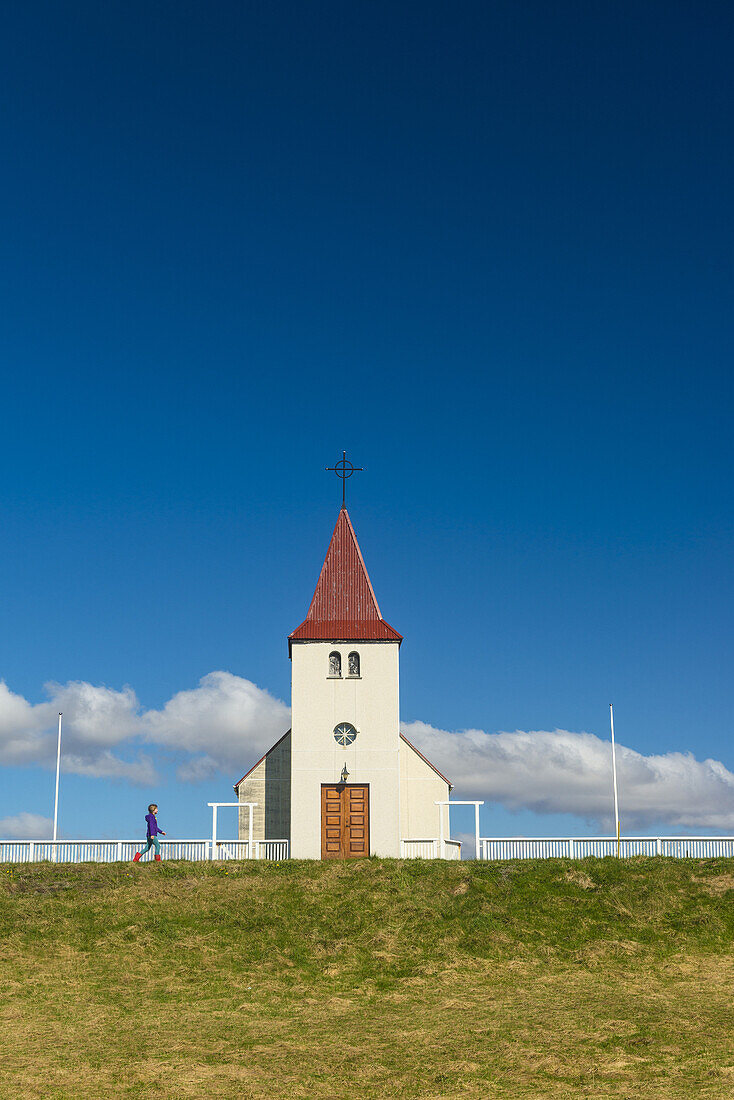 Girl walking past small church; Langaholt, Iceland