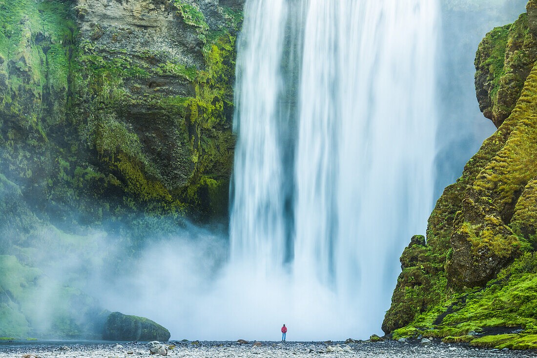 Mann steht am Fuße des Skogafoss-Wasserfalls; Island