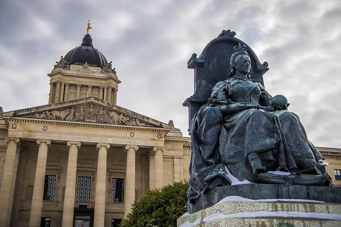 Eine Skulptur von Königin Victoria mit dem Manitoba Legislative Building im Hintergrund und einer Statue des Golden Boy auf der Spitze; Winnipeg, Manitoba, Kanada.