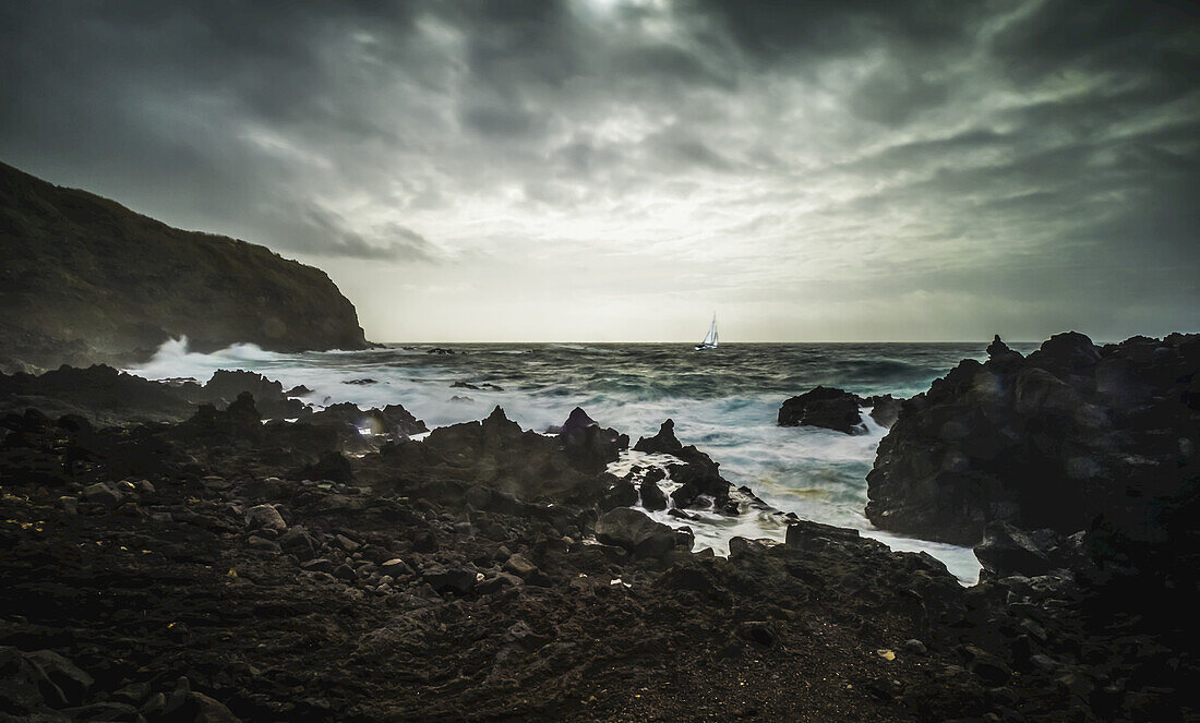 Rugged landscape along the Atlantic coast with a yacht in a storm; Sao Miguel Island, Azores, Portugal