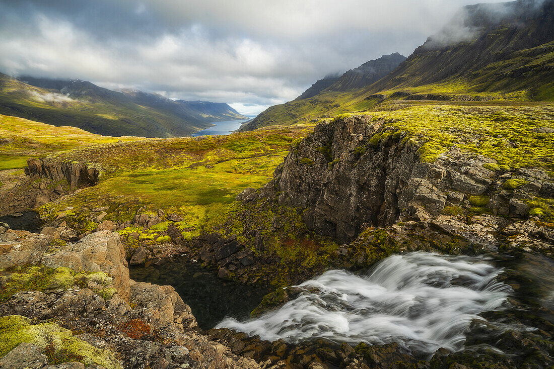 Zerklüftete isländische Landschaft mit leuchtend grüner Tundra und Blick auf die Küstenlinie in der Ferne; Island