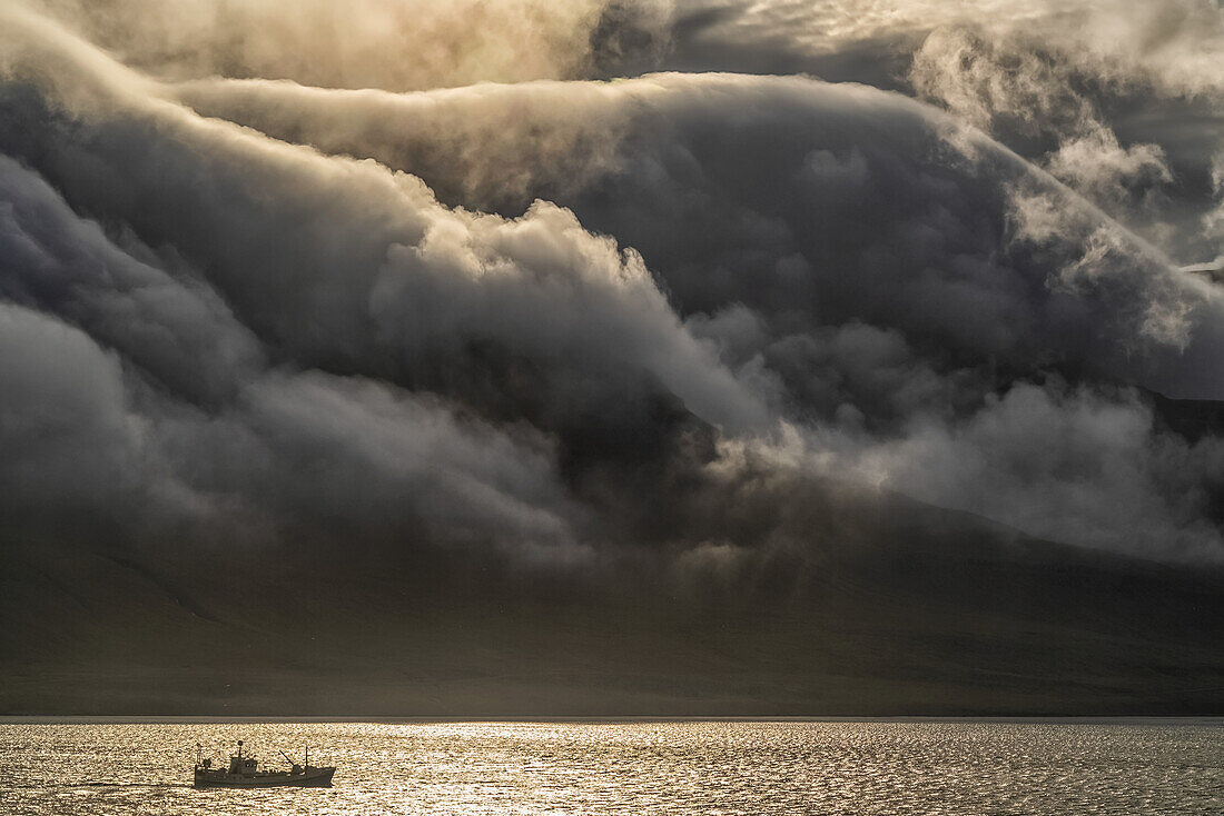 Fischerboot mit dramatischen Wolken, die über die Berge ziehen; Ostfjorde, Island