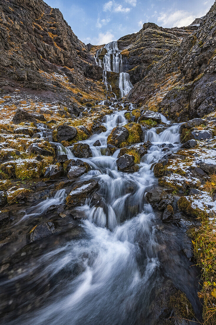 Wasserfall entlang schroffer Felsen mit Flechten und Moos am Wegesrand; Island