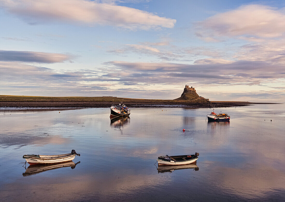 Four fishing boats moored in the harbour with the tide in, Lindisfarne Castle in the background on Holy Island; Lindisfarne, Northumberland, England