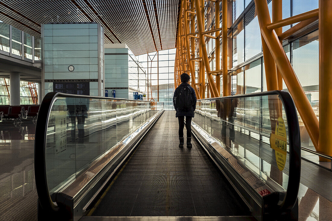 Passagier steht auf dem sich bewegenden Bürgersteig im Terminalgebäude des Flughafens, Beijing Capital International Airport; Beijing, China.