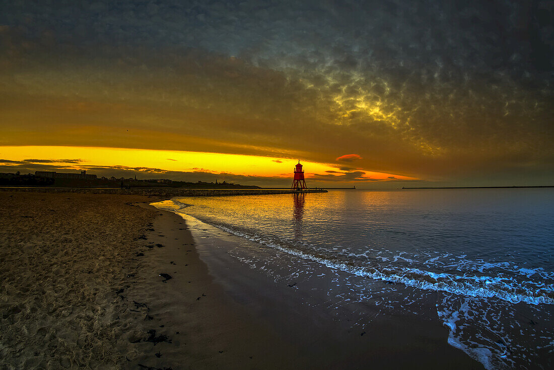 Leuchtturm Herd Groyne, beleuchtet von einem glühenden, goldenen Sonnenuntergang; South Shields, Tyne and Wear, England.