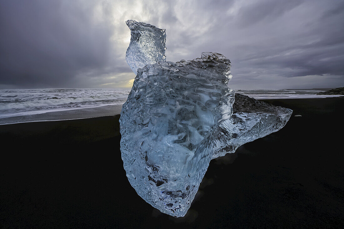 Large chunk of ice sitting on the shore of Iceland with dramatic skies in behind it; Iceland
