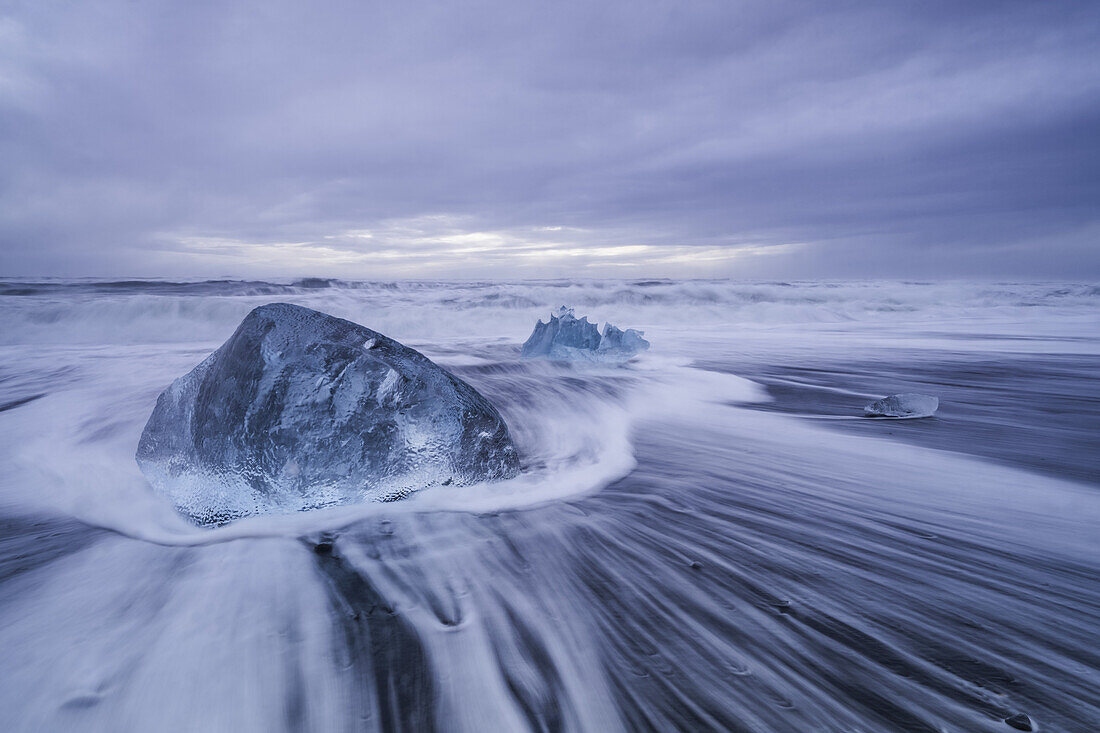 Großer Eisblock, der an der Küste von Südisland liegt, während die Wellen an die Küste schlagen; Island