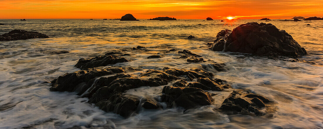 Glowing orange sunset over the Pacific Ocean as viewed over the rock formations from the Oregon coast; Oregon, United States of America